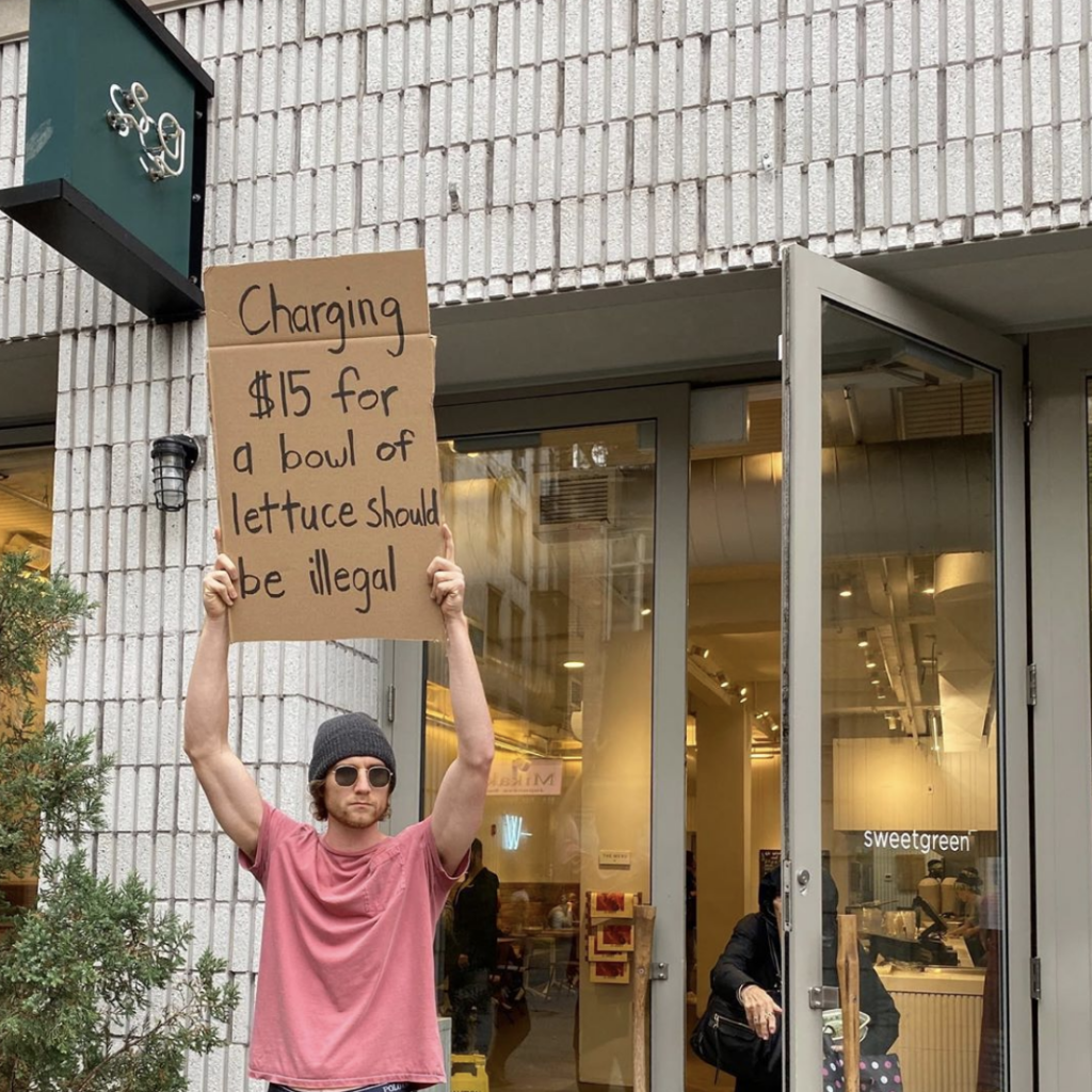 dude with sign holding a sign that reads $15 for a bowl of lettuce should be illegal. Cover photo for post on plant-based on a budget.